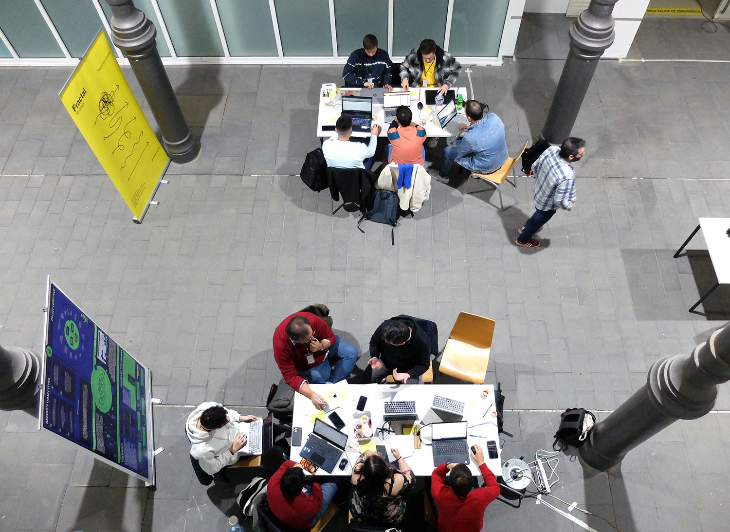 Vista cenital de dos grupos de personas trabajando en torno a sendas mesas, con sus ordenadores