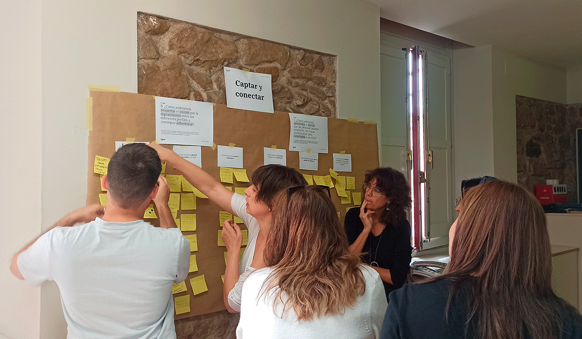 Alguien del equipo ayuda a los participantes a colocar postits en un mural.