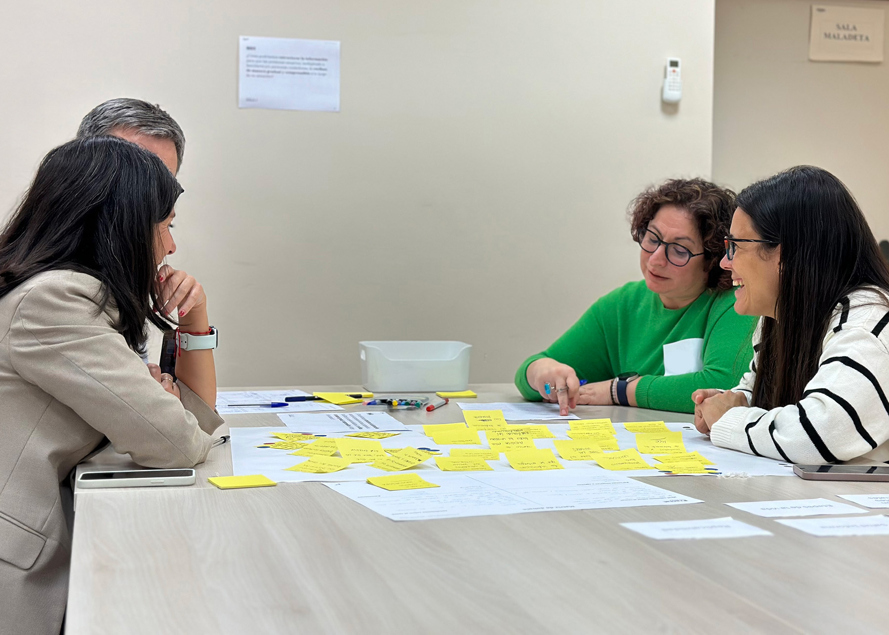 Cuatro personas personas en un taller de cocreación debatiendo sobre un tema con fichas y post-it en una mesa.