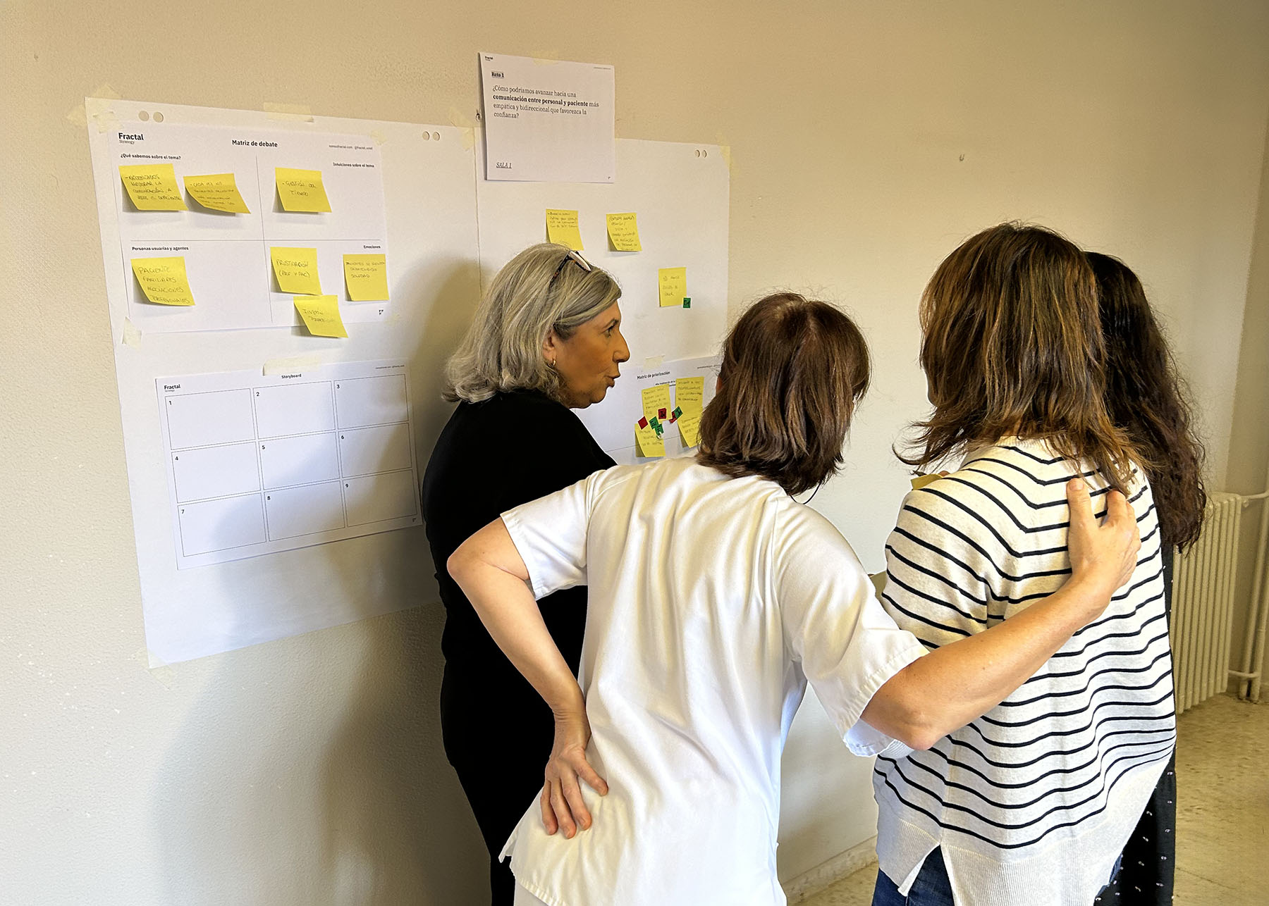 Cuatro personas personas en un taller de cocreación debatiendo sobre un tema con fichas y post-it en la pared.