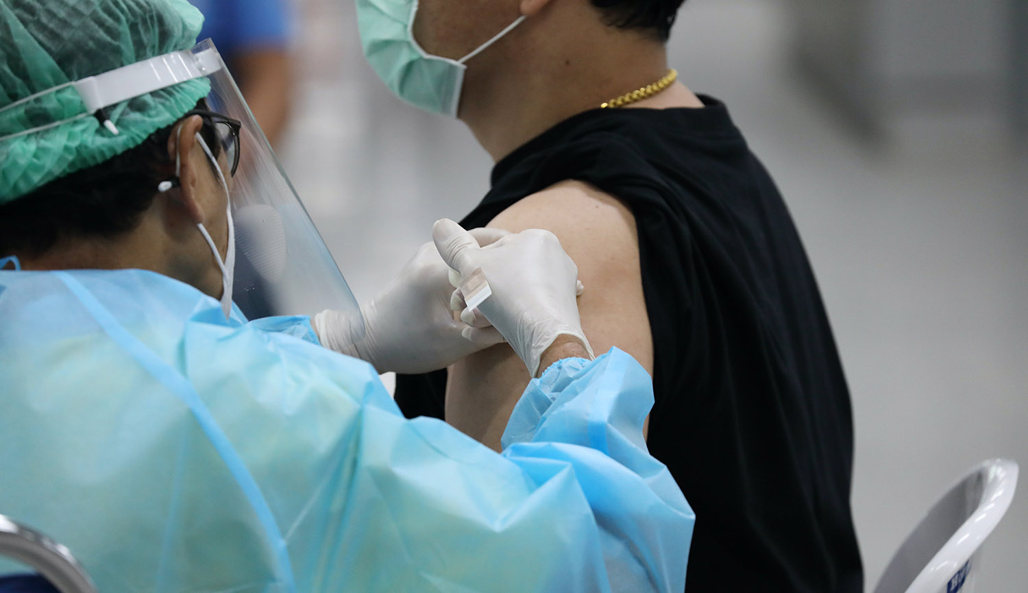 Una persona sanitaria con equipos de protección individual inyecta en el brazo a un hombre con mascarilla