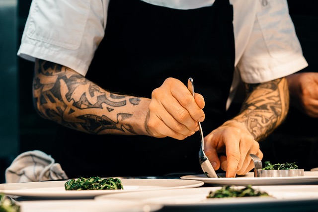 Unas manos con brazos tatuados emplatan en lo que parece una cocina de un restaurante